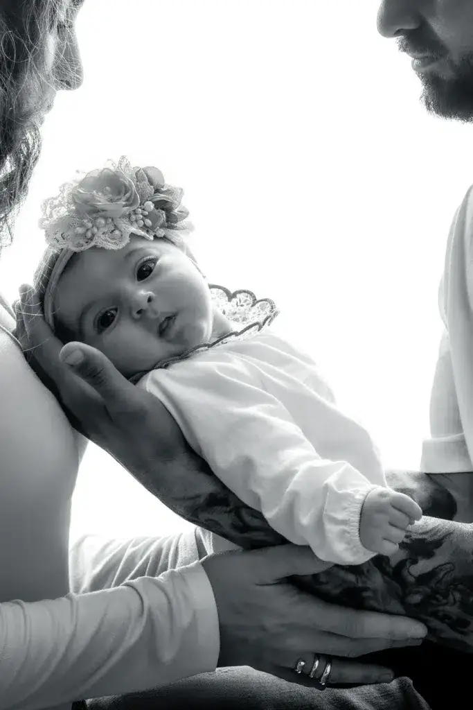Bebé recién nacida sostenida por sus padres, en blanco y negro.
