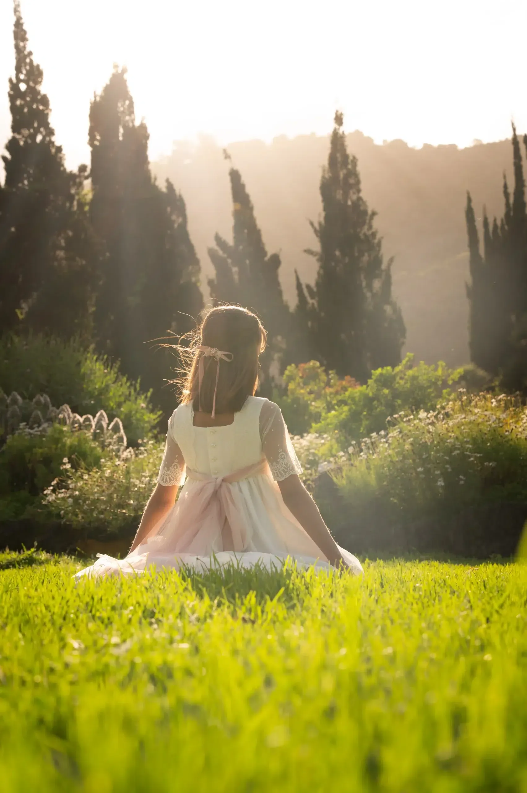 Niña con vestido de comunión en un jardín lleno de luz.