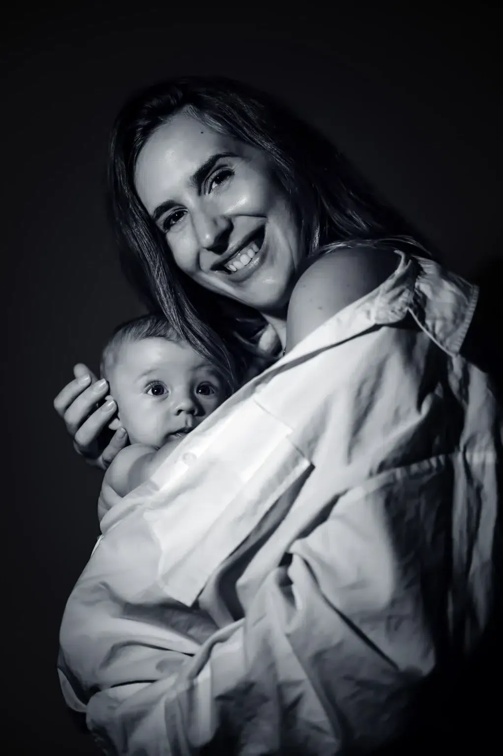 Una madre sonríe mientras sostiene a su bebé en un retrato en blanco y negro.