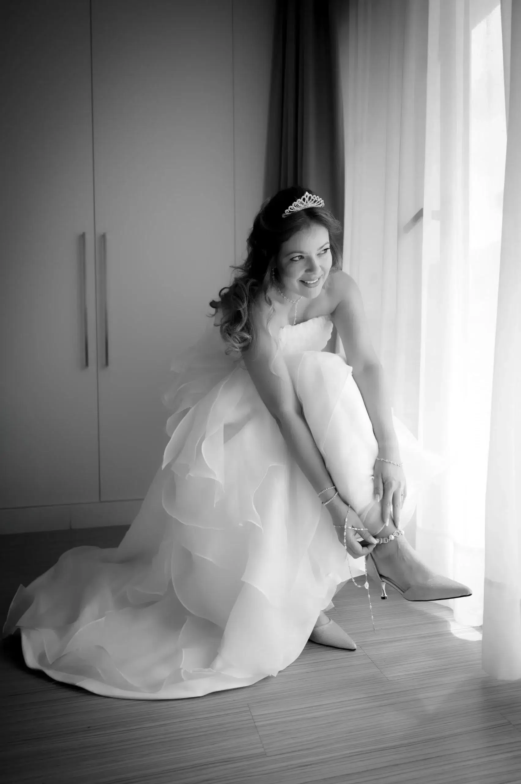 Novia poniéndose los zapatos junto a una ventana durante sus preparativos.